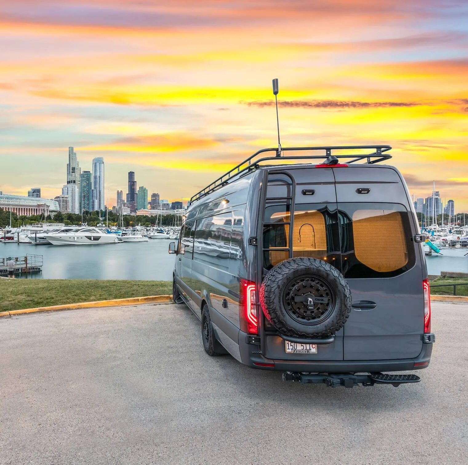 A Highland Vans Sprinter parked on the Chicago lakefront at sunset, its rear doors open on a wood interior, with the city skyline and a marina behind it