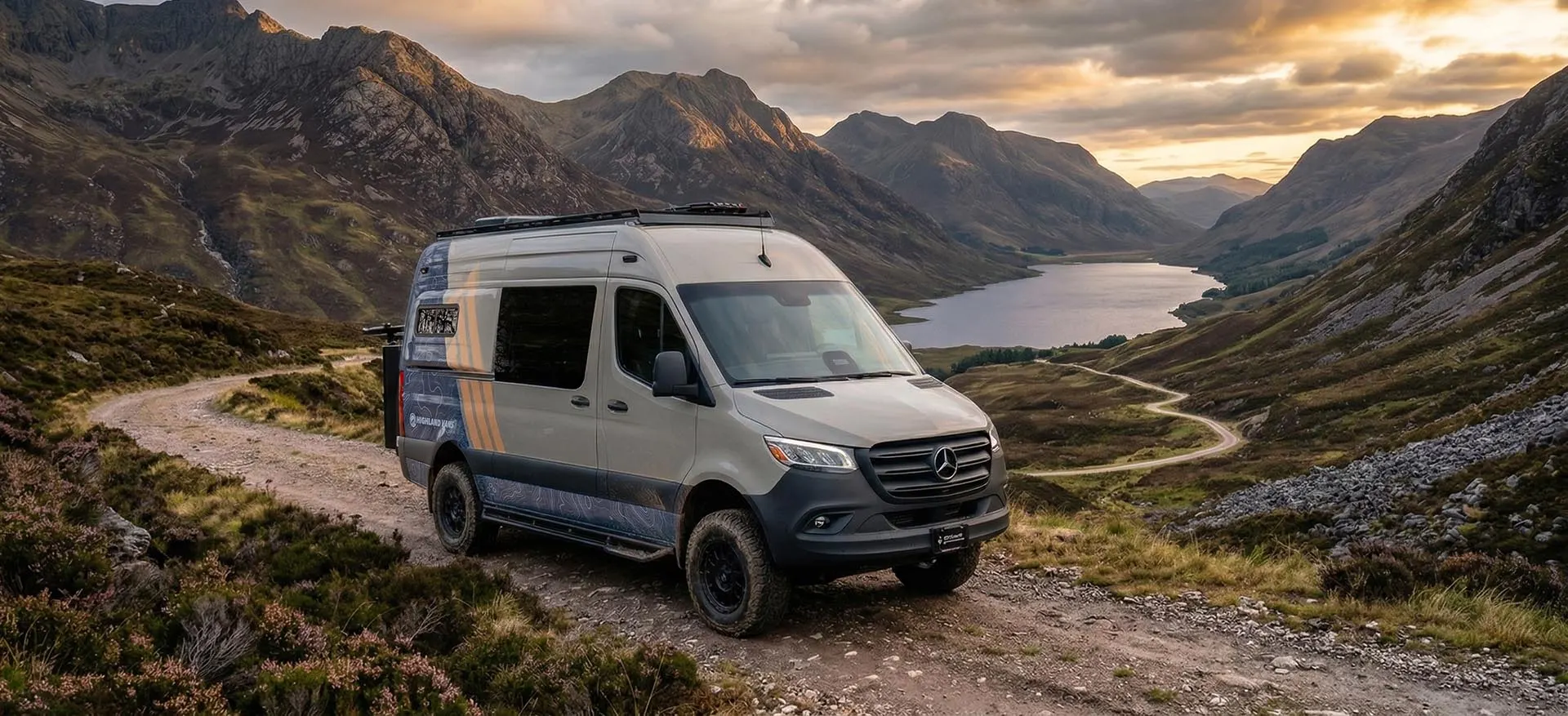 A Highland Vans Sprinter on a single-track gravel road high above a loch, mountains and a sunset behind it