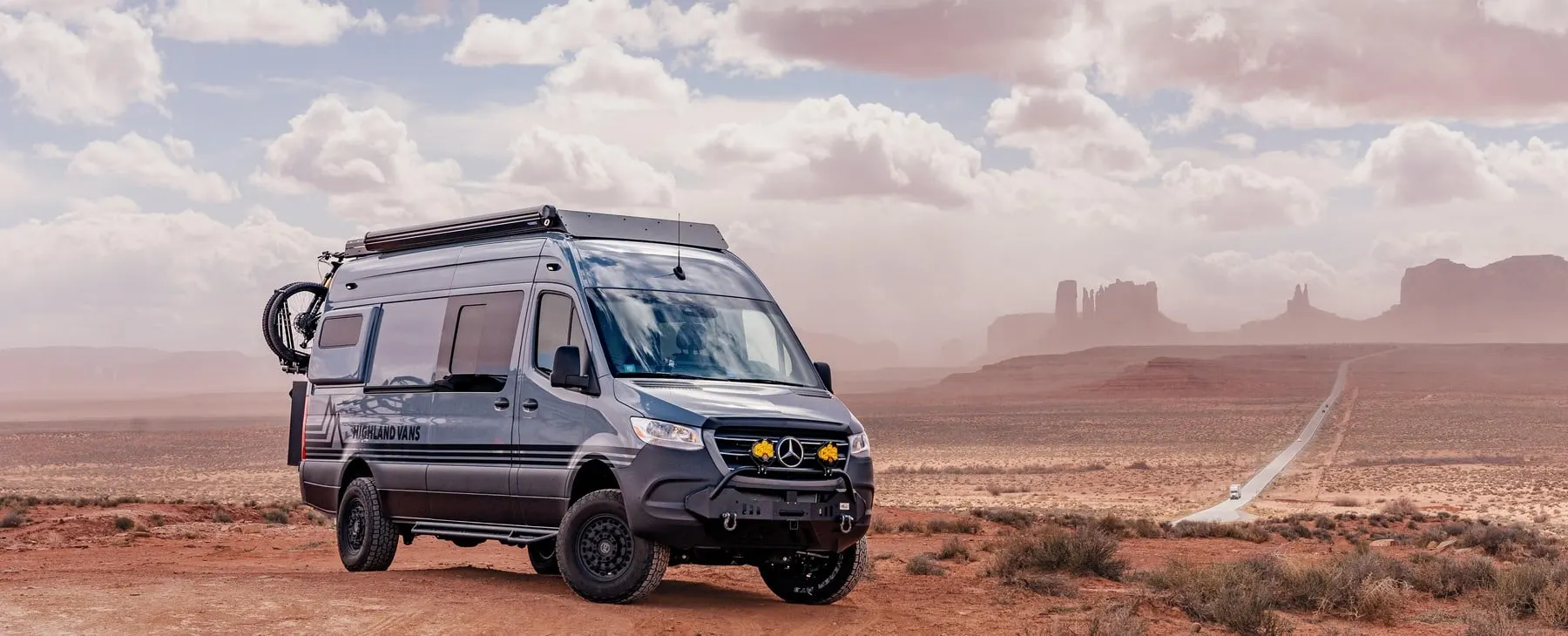 A Highland Vans Sprinter conversion parked on a gravel shoulder at dusk, its side door open to the interior lights