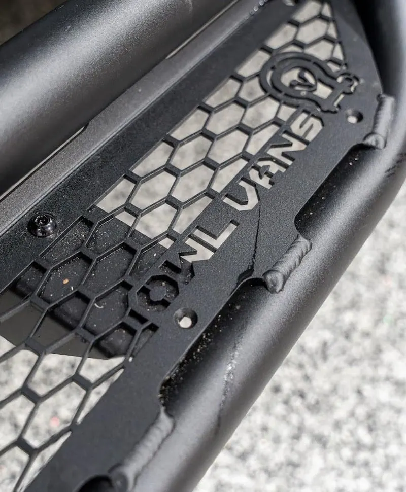 A close view of a black powder-coated Owl Vans side step, its honeycomb tread plate wet from the road