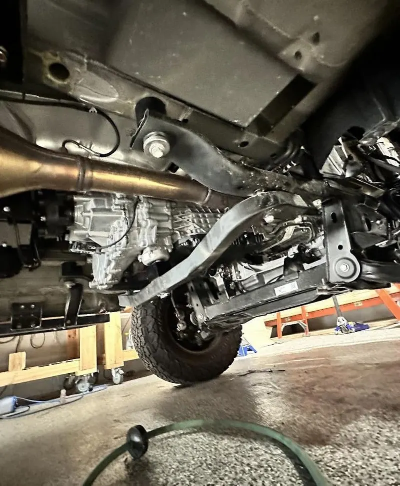 The underside of a Sprinter on shop stands, showing the transfer case, the exhaust and the skid armour bolted across the chassis rails