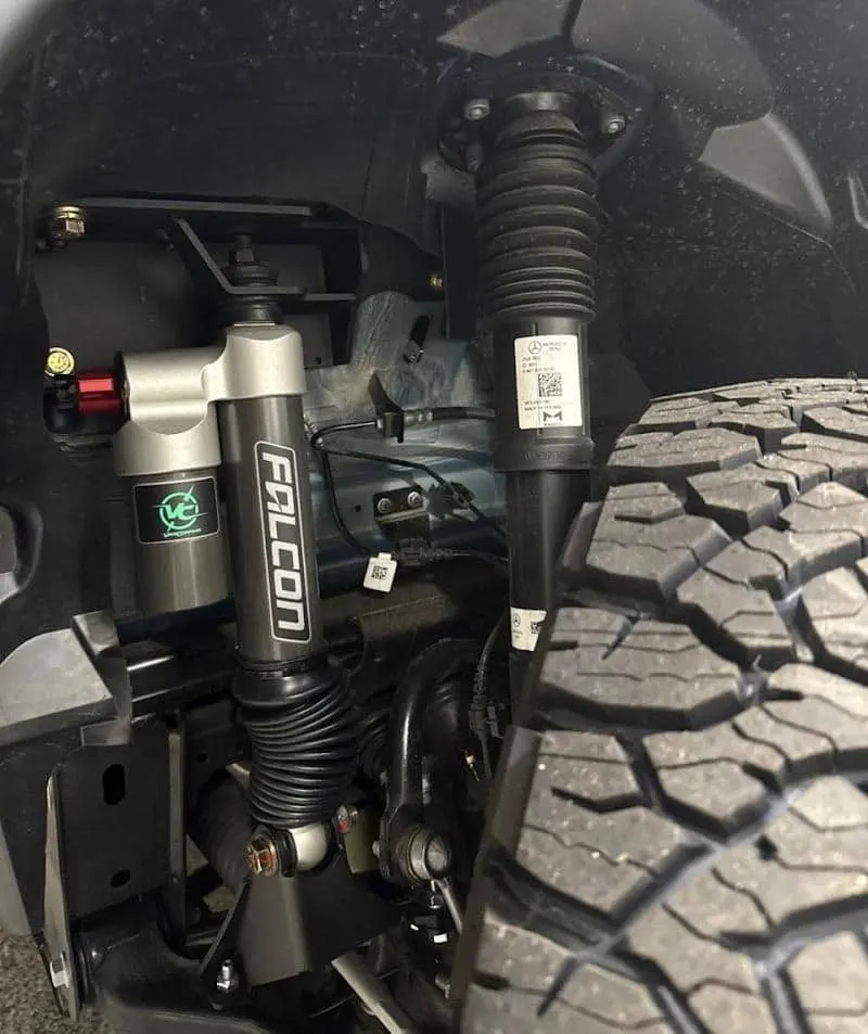 A VanCompass Falcon shock and the factory strut in a front wheel arch, beside an all-terrain tyre