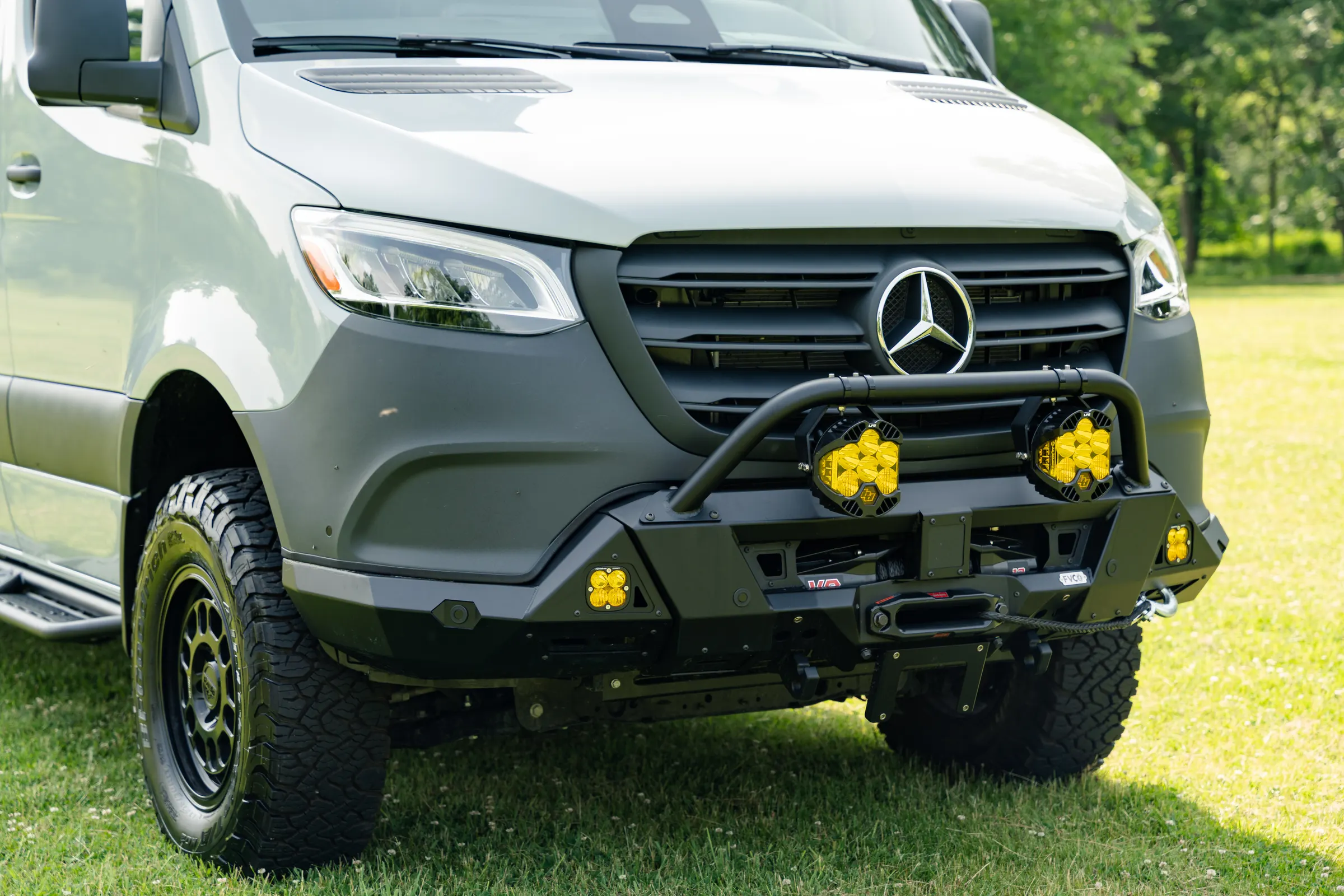 Front three-quarter close view of the steel bull bar, the winch behind it, four yellow-lensed auxiliary lights and an all-terrain tyre on a black wheel