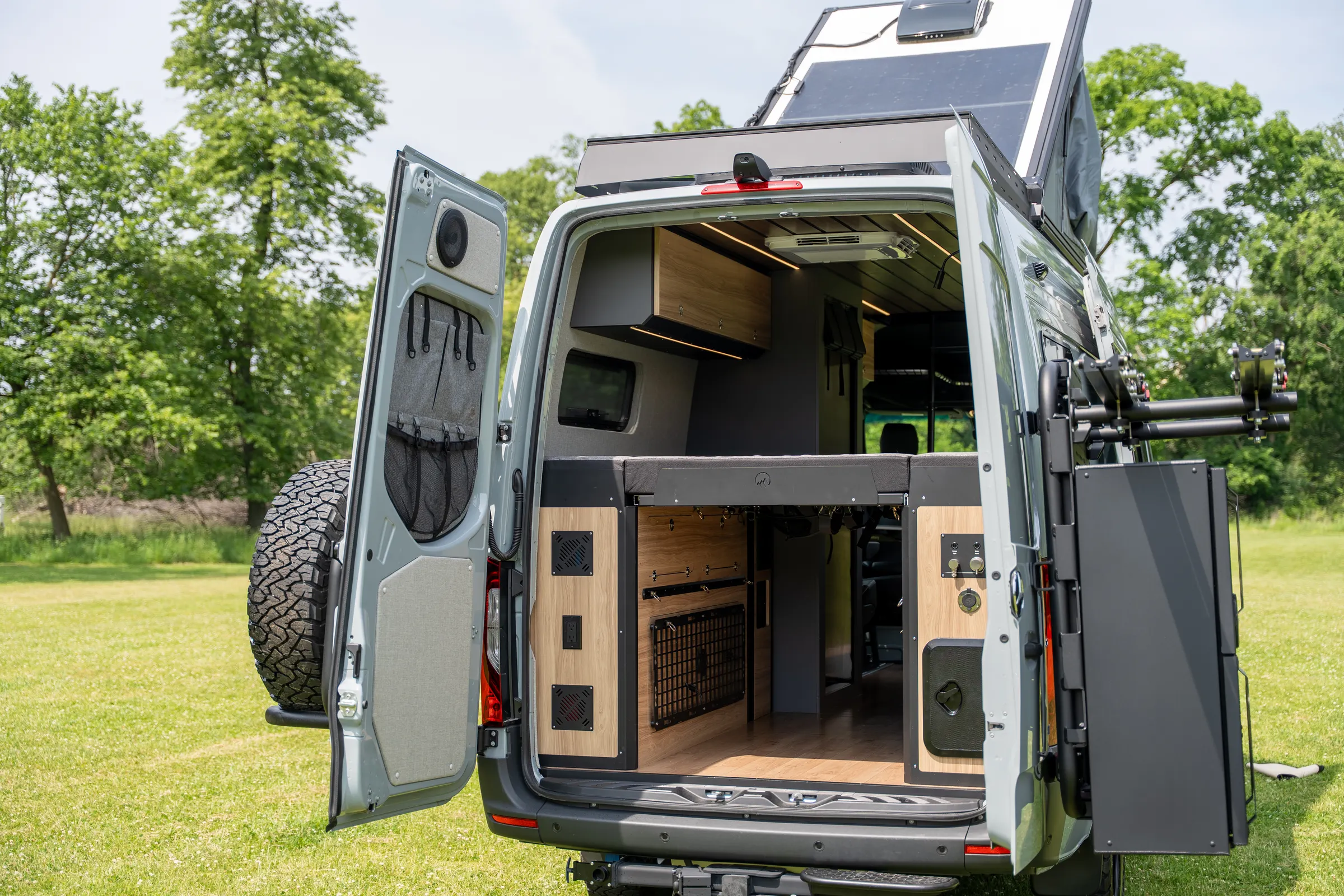 Both rear doors swung wide onto the gear garage under the bed: lockers with mesh fronts, organiser pockets on one door, a perforated panel on the other, and the roof solar panel above
