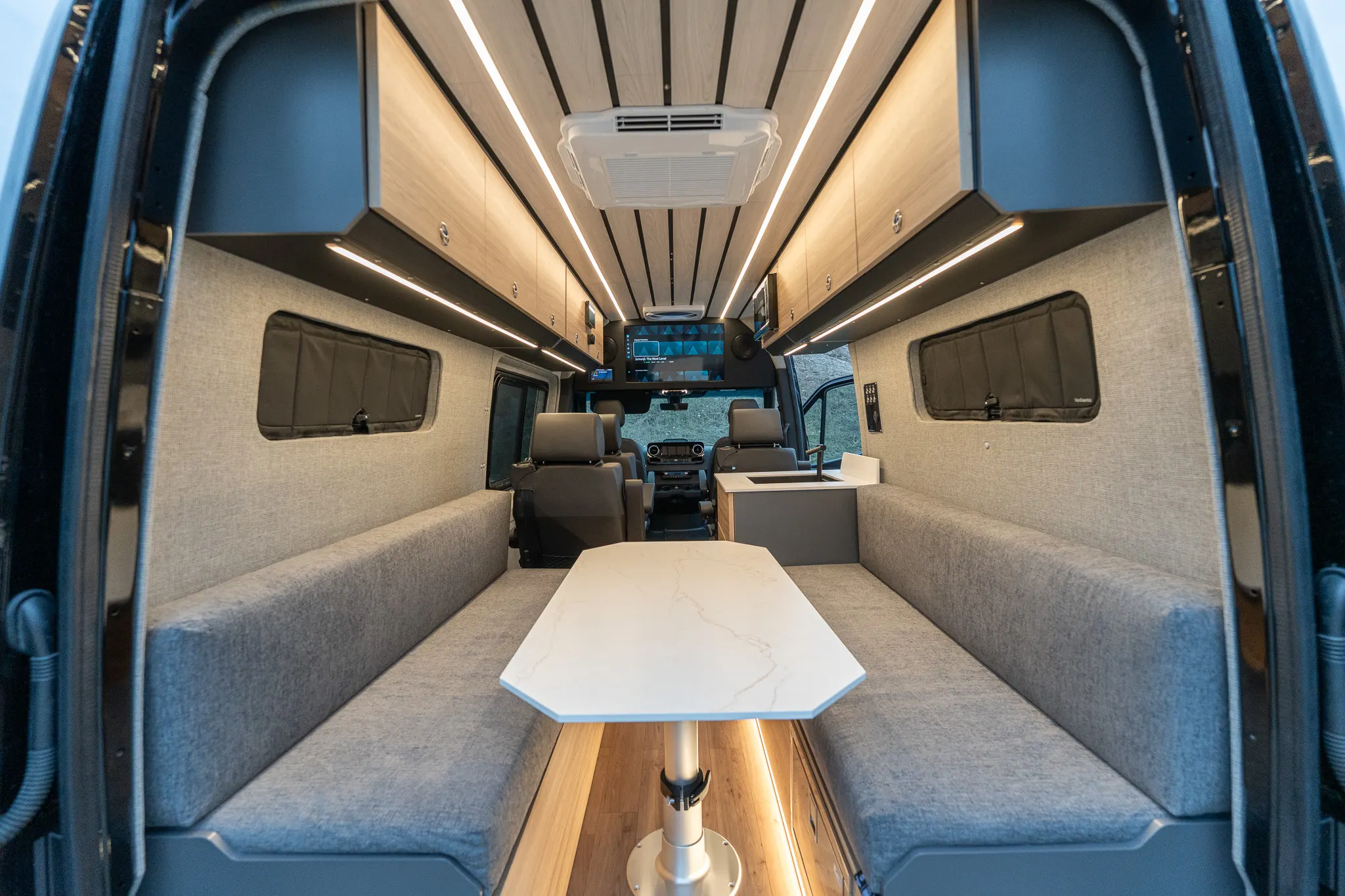 Looking into the Kinabalu through the open rear doors: two facing bench seats around a stone-topped table, overhead cabinets, the ceiling air conditioner and the galley beyond
