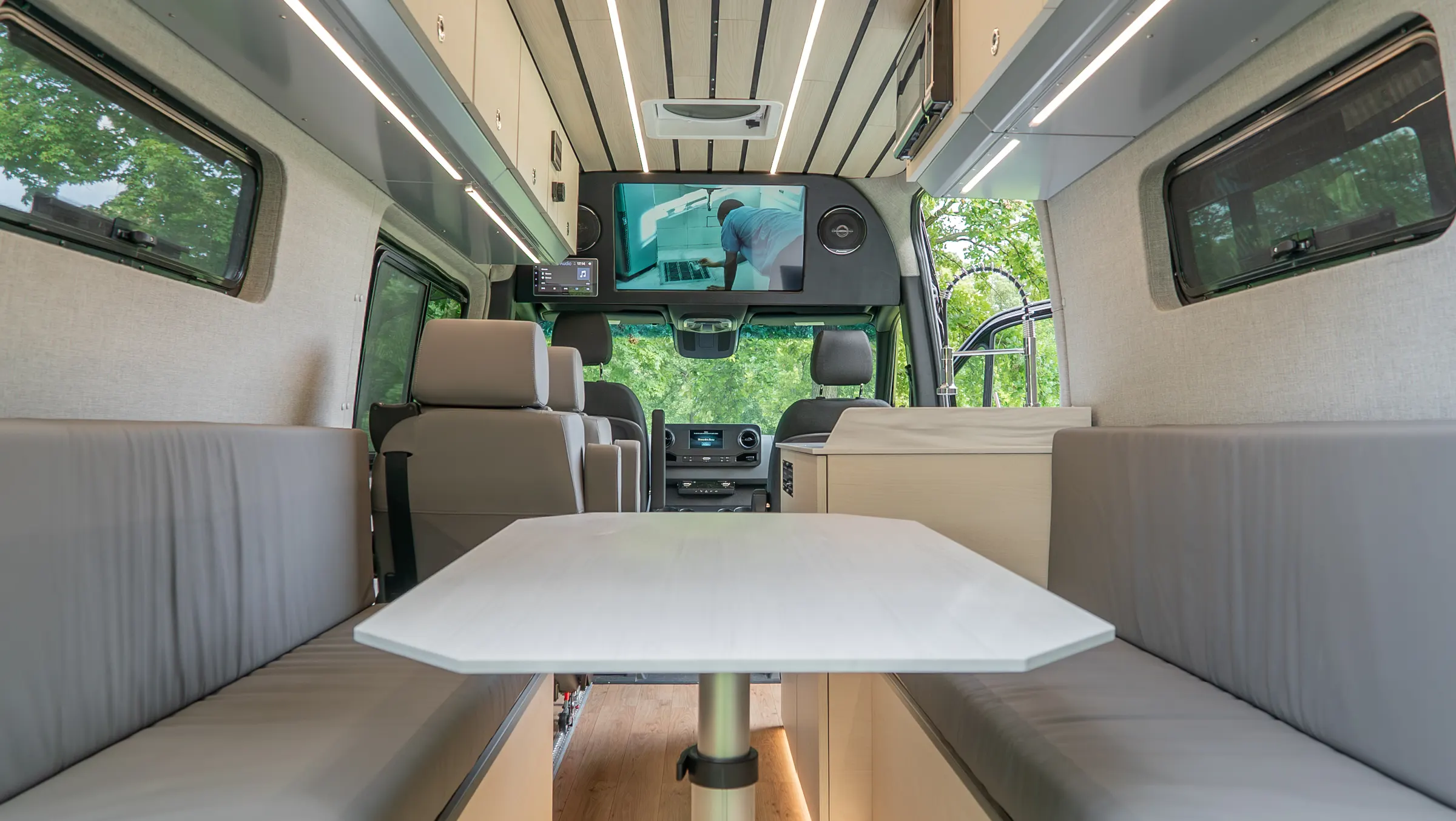 Rear dinette: two facing bench seats and a wide table between them, looking forward past the galley to the screen above the cab