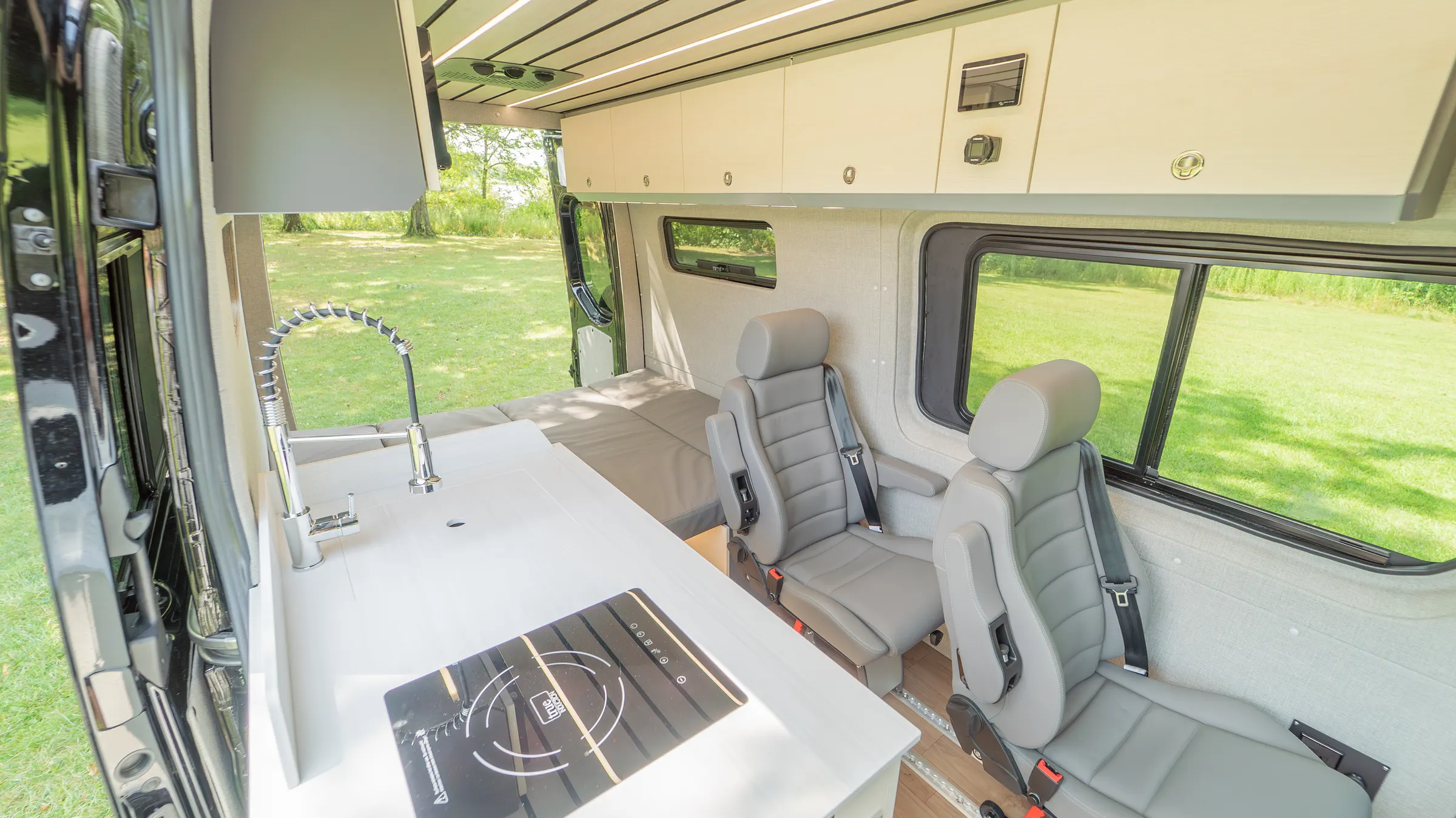 Galley counter with a flush induction cooktop and a pull-down faucet, the sliding door open onto grass and two belted seats behind it