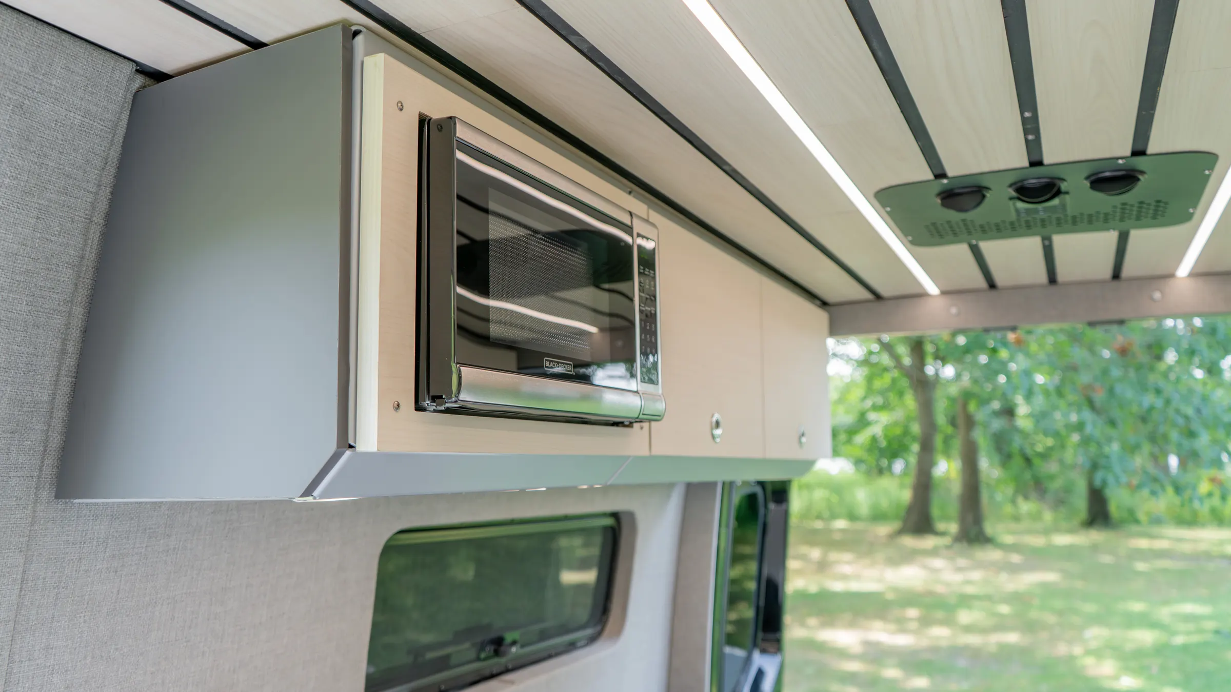 Microwave built into the overhead cabinet run above the sliding door, with the door open onto trees and the roof fan set into the ceiling