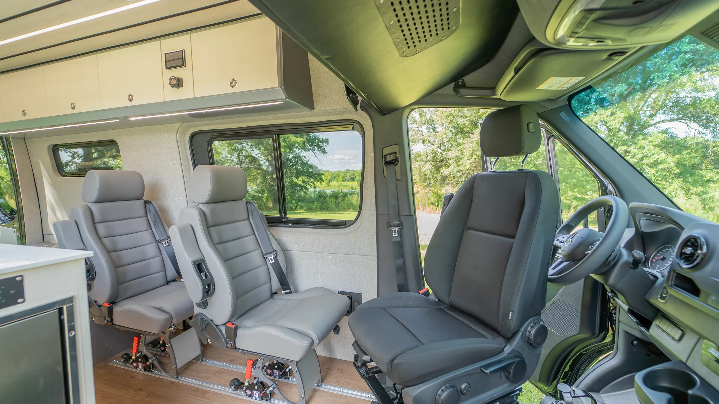 Two belted seats on floor rails behind the cab, looking forward past the driver's seat to the steering wheel