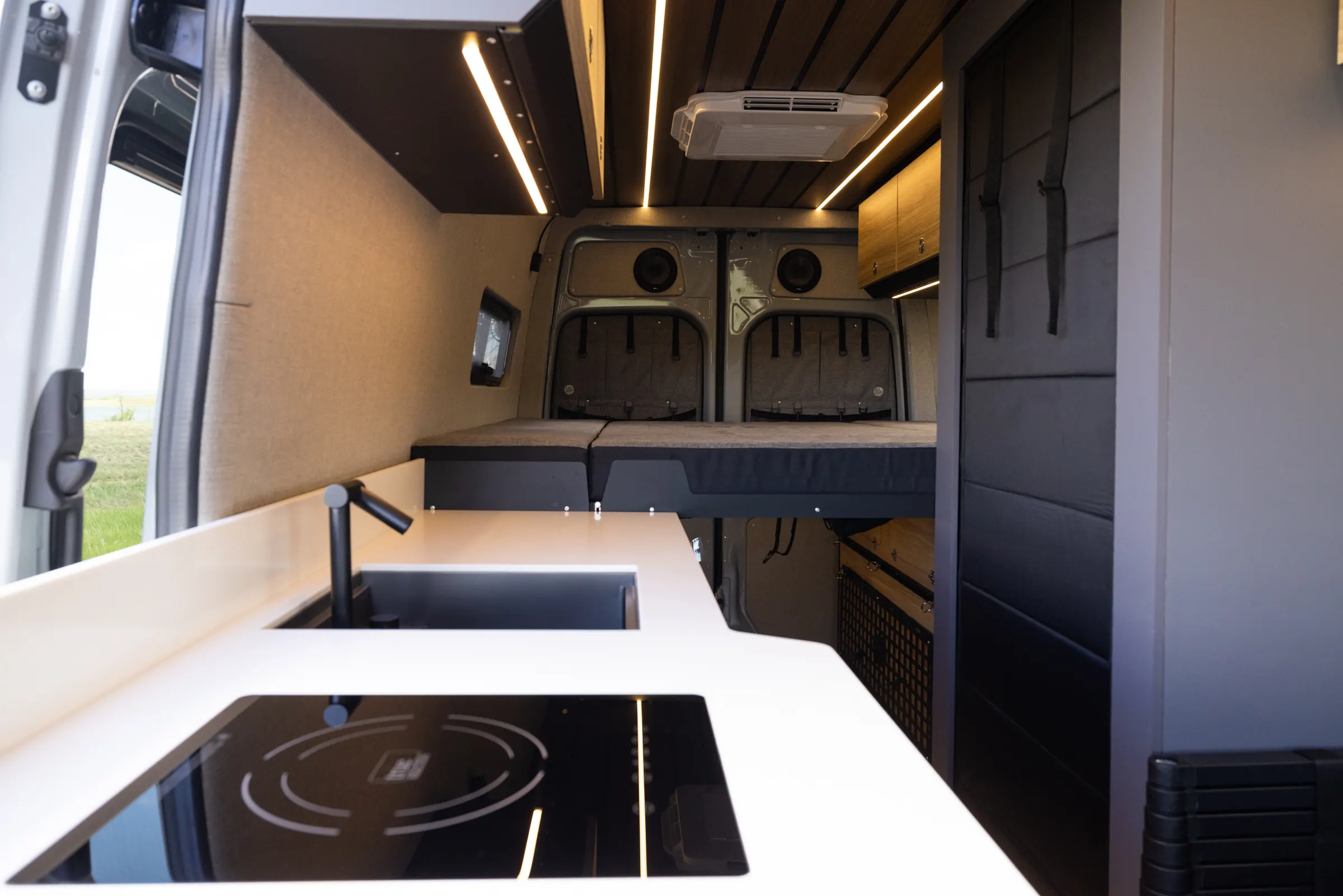 Galley worktop looking aft, with a flush induction hob and a pull-down faucet over an undermount sink, the rear bed made up beyond it and a low-profile air conditioner set into the slatted ceiling