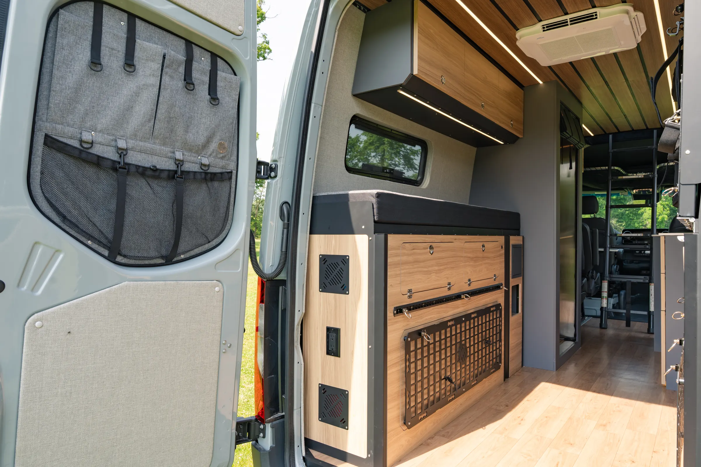 The sliding door open from outside, showing mesh organiser pockets on the door, a locker with a mesh front beside a switch and outlet panel, and the cab seats through the cabin beyond