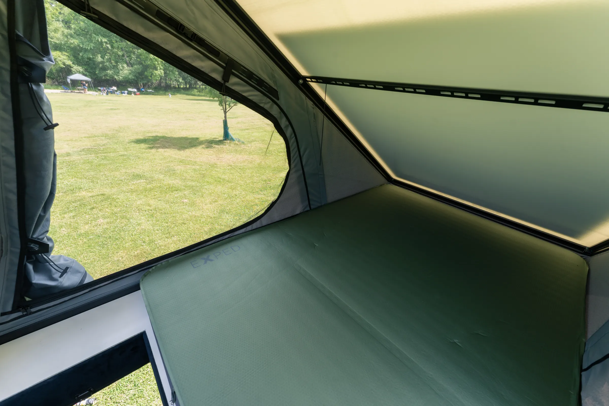 Inside the pop-top roof tent, the mattress laid across it and a wide mesh window looking out over grass and trees