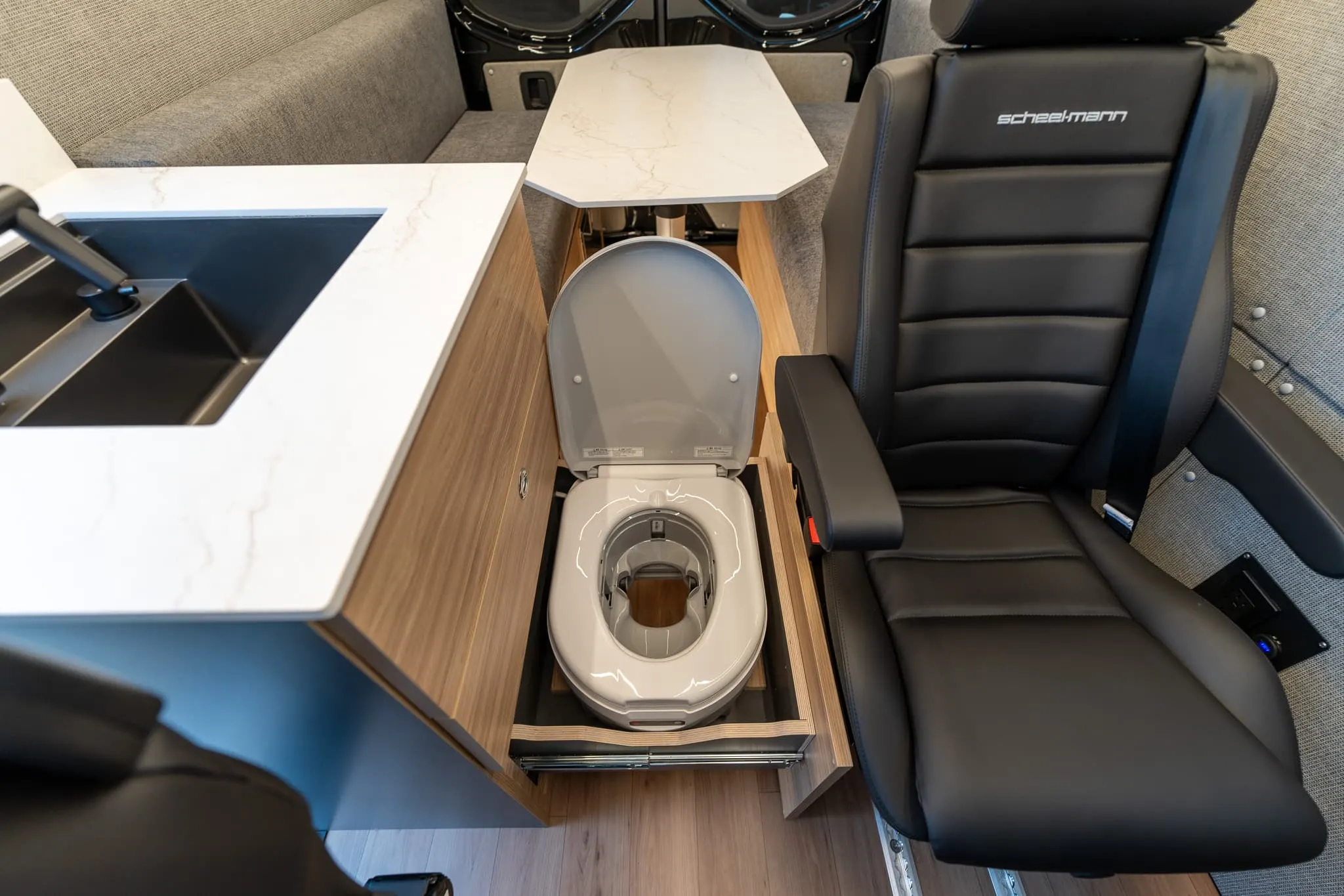 Dry-flush toilet on a pull-out drawer in the cabinet beside the galley, lid open, with the passenger seat alongside it
