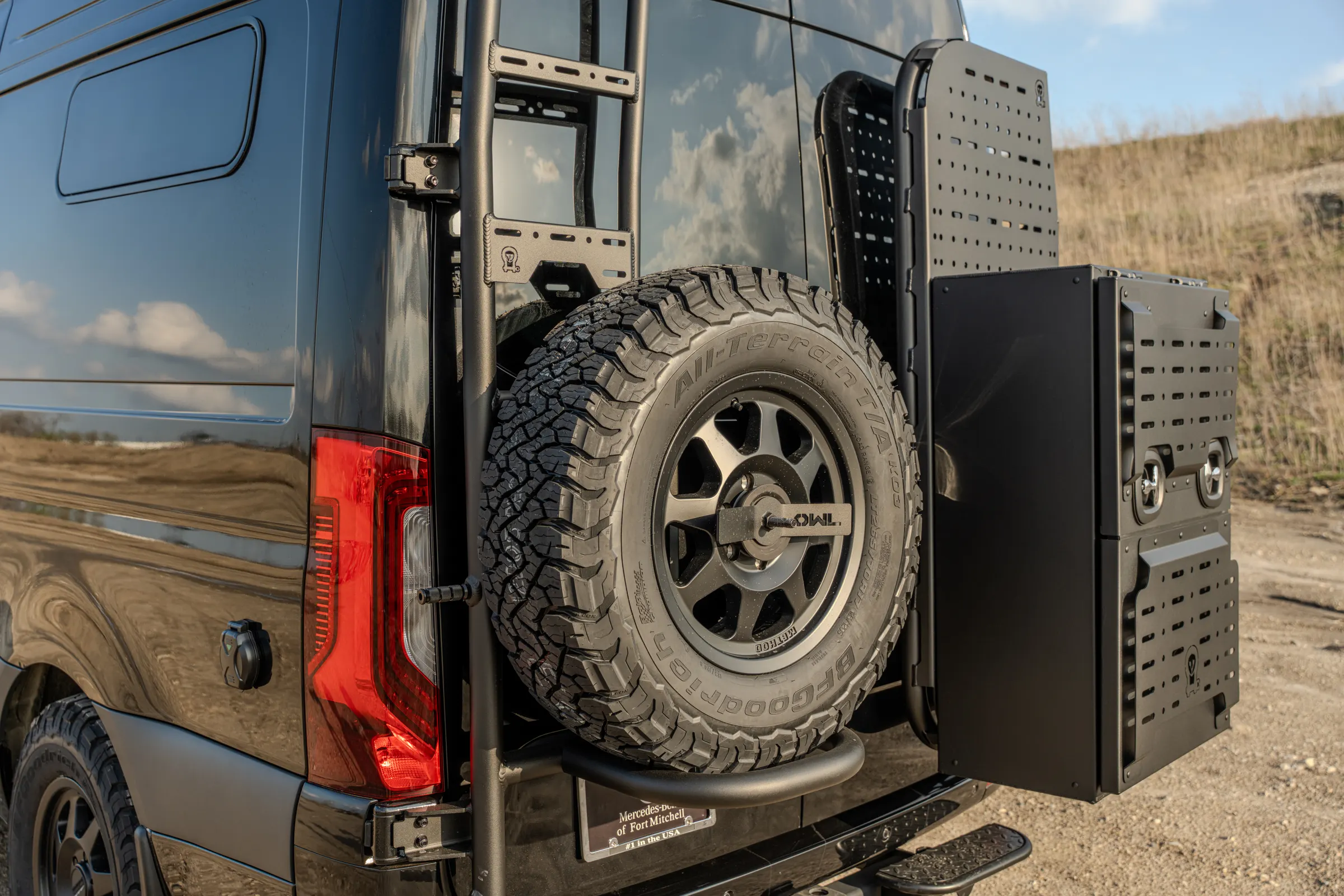 Close view of the rear door gear: the spare wheel on its swing-out arm, perforated gear panels and the cargo box behind them