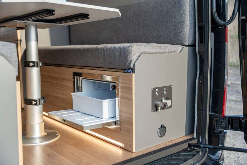 Campervan galley kitchen featuring a 12V compressor refrigerator, induction cooktop, and premium storage cabinets